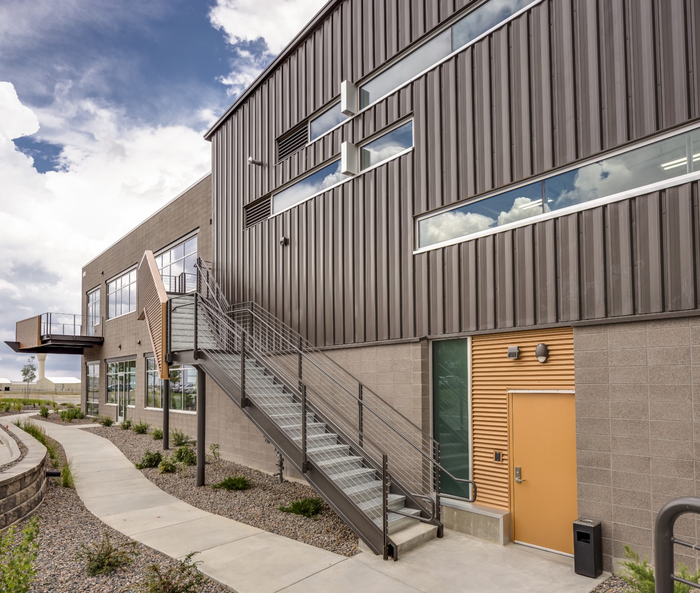 Two-story commercial facility featuring vertical metal wall panels, concrete block lower walls, and an exterior metal stair system.